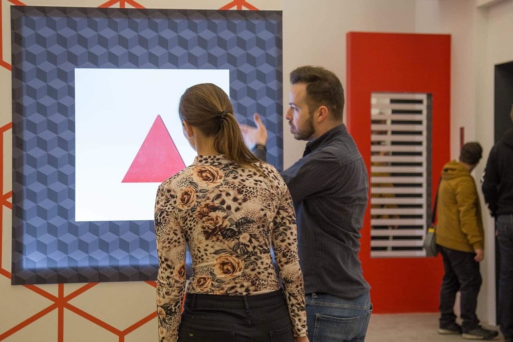 Egy nő és egy férfi figyeli a geometrikus mintákat ábrázoló digitális művészeti kijelzőt.